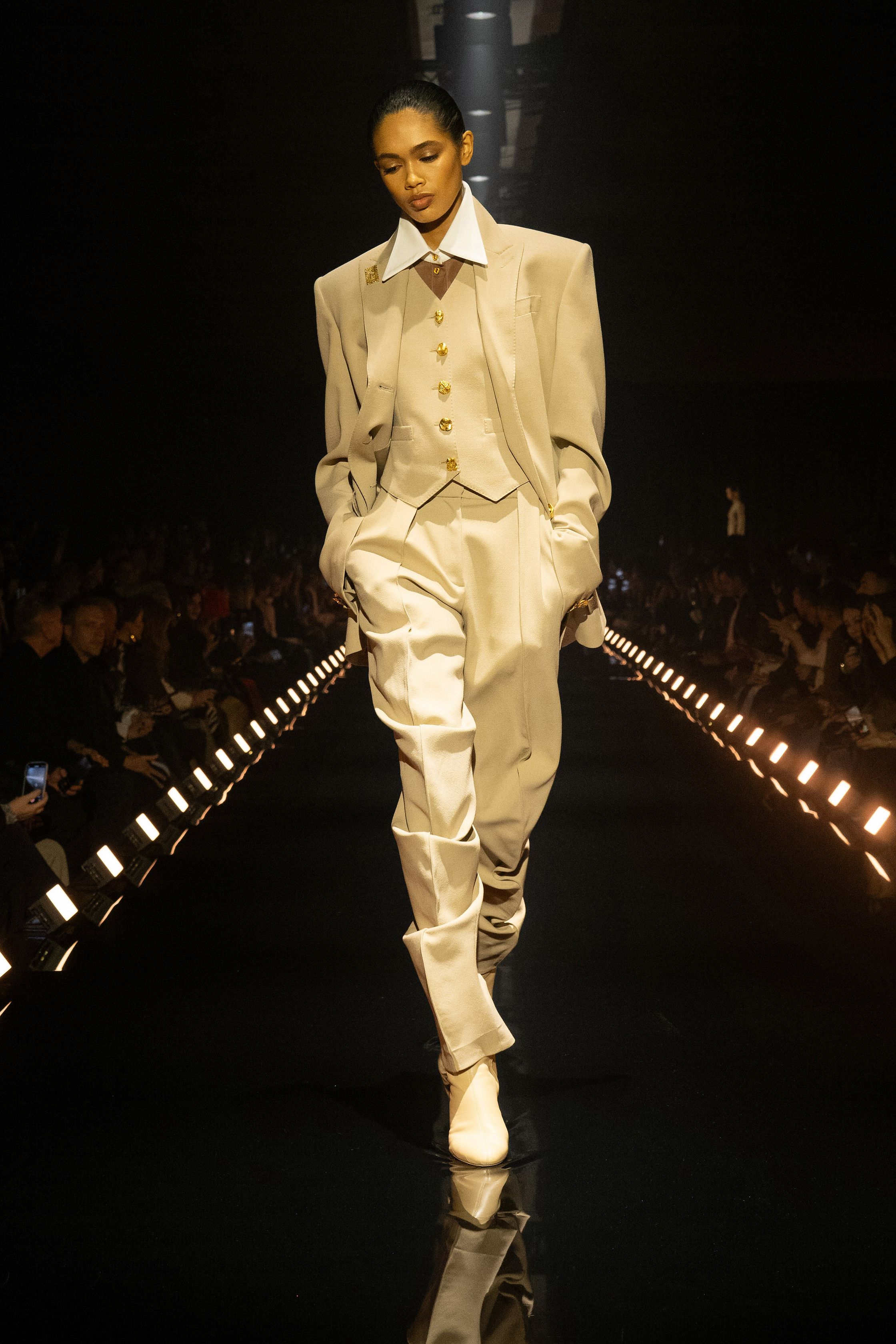 Schiaparelli 2026秋冬系列延续品牌标志性的超现实主义美学，在金色灯光的T台上呈现极具雕塑感的廓形。沙金色与黑金色成为主调，褶皱礼服、雕塑式西装与高腰裙装强化身体线条。经典的金属装饰、夸张肩线以及精致刺绣细节构成强烈视觉符号，使整场秀既华丽又充满戏剧张力。设计师通过结构与面料的张力对比，让高级定制的艺术精神融入现代女性衣橱-顽石频道趋势研究